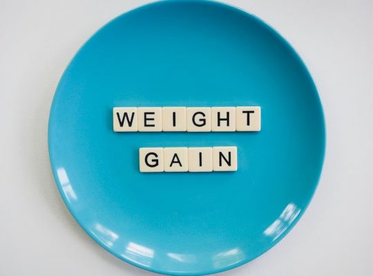 Scrabble tiles spelling 'weight gain' on a blue plate, symbolizing health and diet.