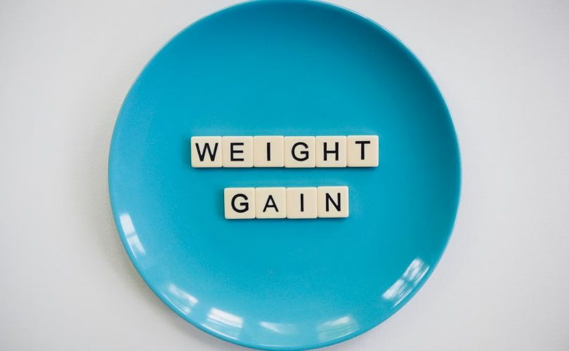 Scrabble tiles spelling 'weight gain' on a blue plate, symbolizing health and diet.