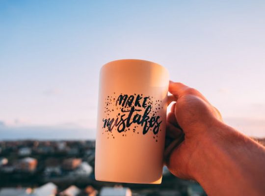 A hand holding a motivational mug with 'Make Mistakes' against a sunset in Lviv.