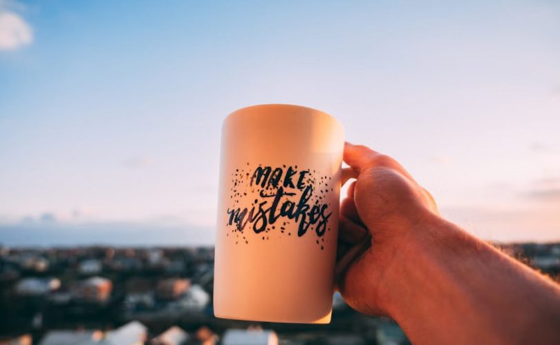 A hand holding a motivational mug with 'Make Mistakes' against a sunset in Lviv.